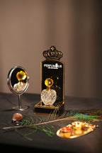 A crystal-cut designer bottle of Fragrance of Faith Attar by Perfumous, styled with a peacock feather and ritual lamps.