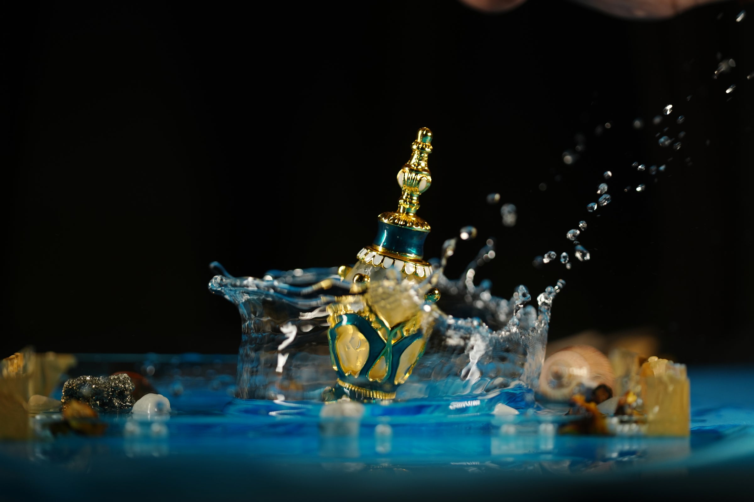 A teal and gold designer bottle of Liquid Luck Attar by Perfumous splashing in water, representing a fresh surge of success.